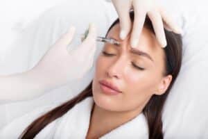 Young woman receiving an anti-aging Botox filler injection in her forehead from a professional cosmetologist at a beauty salon