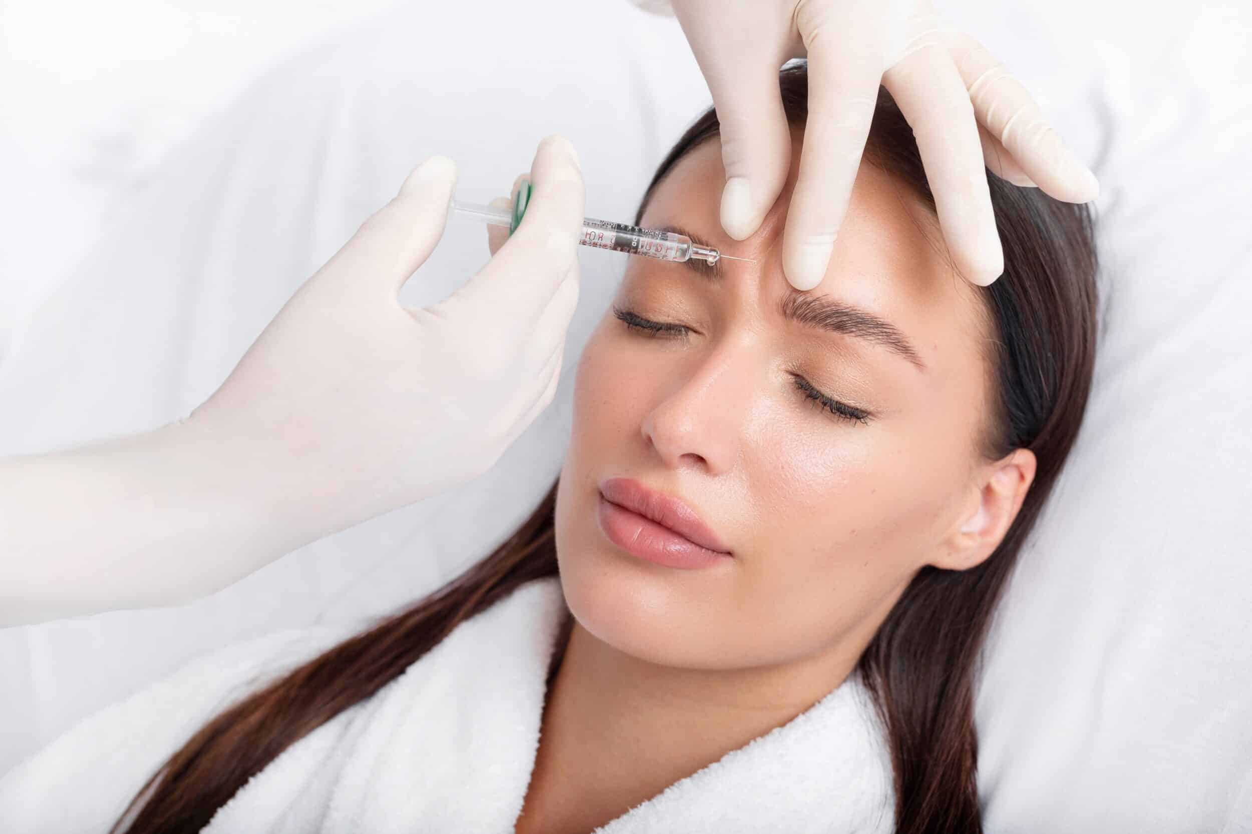 Young woman receiving an anti-aging Botox filler injection in her forehead from a professional cosmetologist at a beauty salon