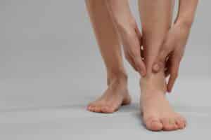 Close-up of woman holding her leg in pain on gray background, concept of muscle strain, leg discomfort, and pain relief