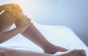 Woman touching her swollen lower leg while sitting on a bed.