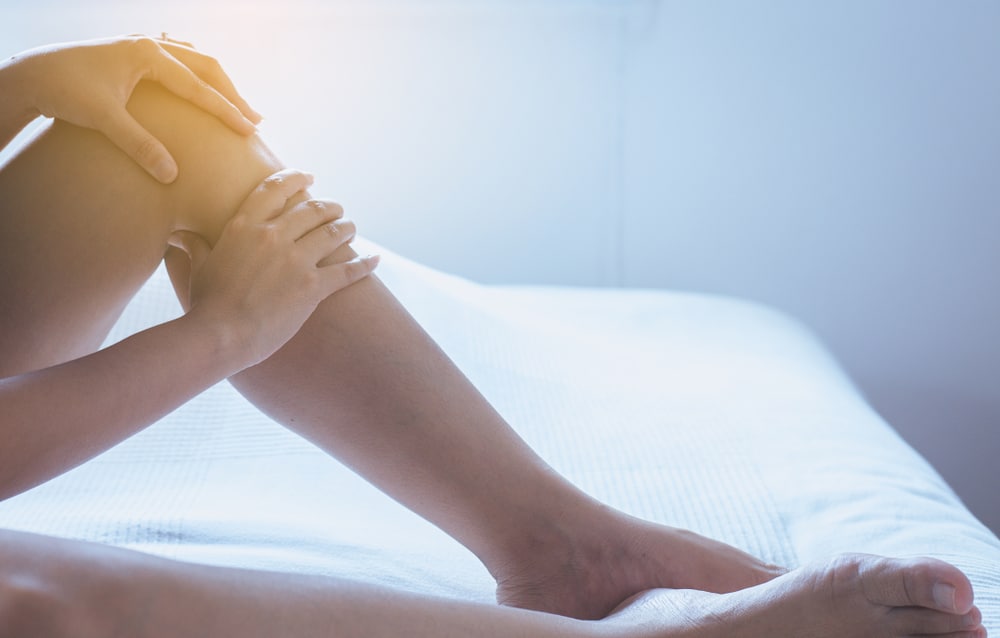 Woman touching her swollen lower leg while sitting on a bed.